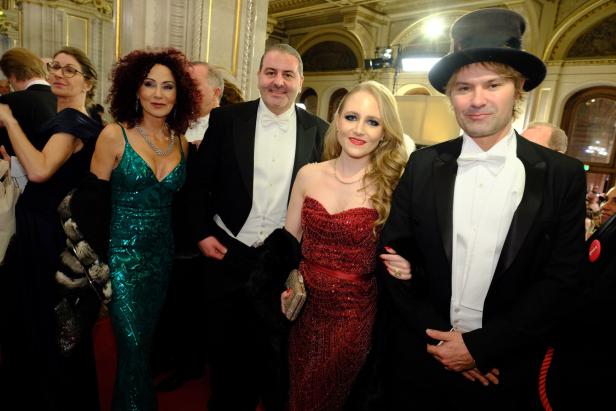 Vier elegant gekleidete Personen posieren in festlicher Umgebung, zwei Frauen in Abendkleidern, zwei Männer im Frack.