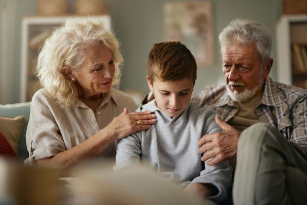 Ein Junge sitzt traurig zwischen seinen tröstenden Großeltern auf einer Couch