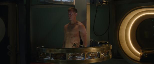 Eine Szene aus "Murderbot": Ein Mann (Alexander Skarsgård) mit Narben am Oberkörper steht in einer futuristischen Apparatur mit sichtbaren Kabeln.