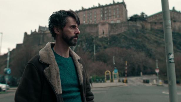 Ein Mann mit Bart und Winterjacke steht vor Edinburgh Castle.