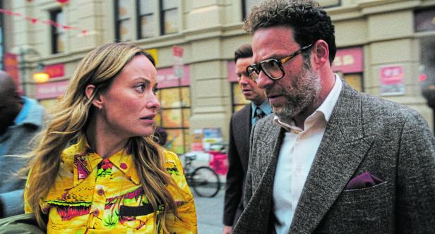 Eine Frau im bunten Hemd und ein Mann im Anzug gehen nebeneinander durch eine belebte Stadtstraße.