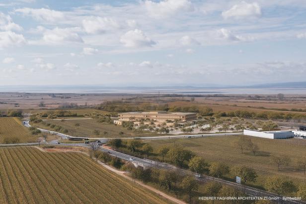 Ein modernes, flaches Gebäude liegt umgeben von Feldern und Bäumen in einer weiten, ländlichen Landschaft.