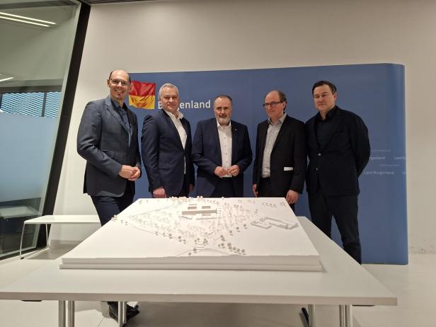 Fünf Männer im Anzug stehen hinter einem Architekturmodell auf einem Tisch vor einer blauen Wand mit Burgenland-Logo.