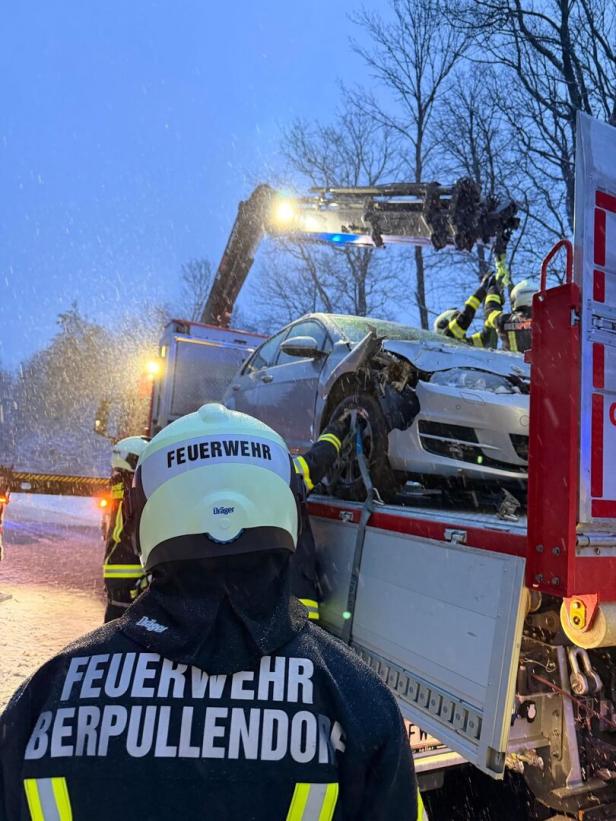 Feuerwehrleute bergen bei Schneefall ein beschädigtes Auto mit einem Kran von einem Lkw.