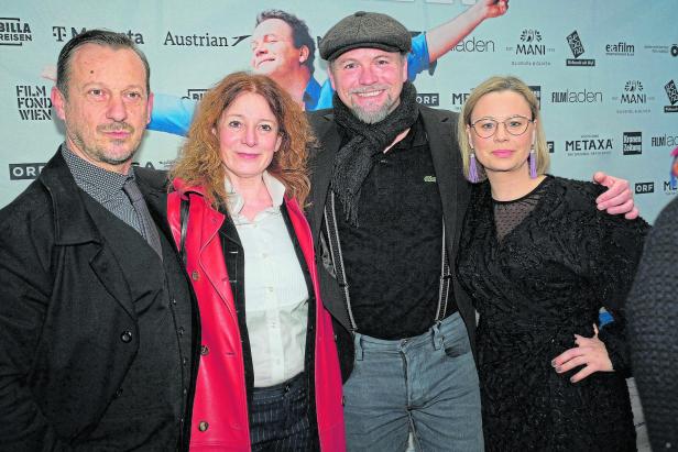 Vier Erwachsene stehen nebeneinander und lächeln in die Kamera, im Hintergrund sind Sponsorenlogos zu sehen.