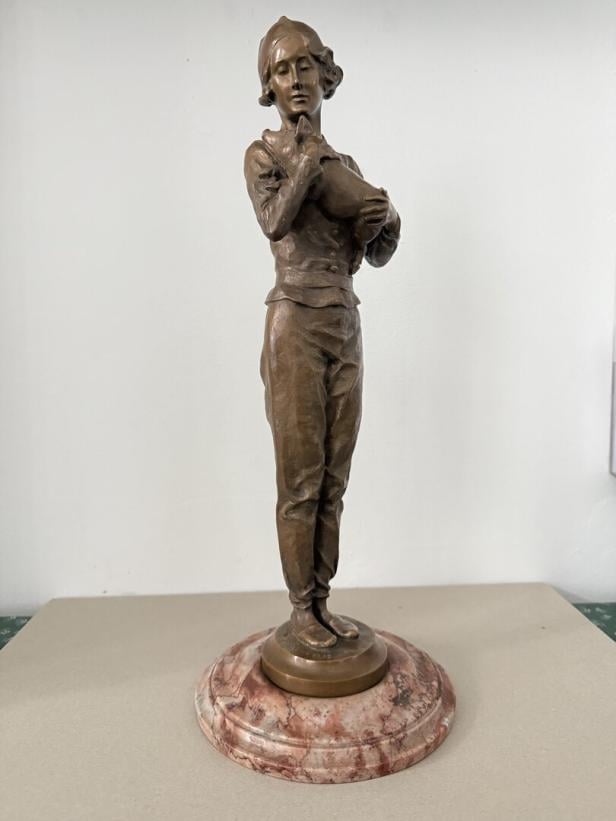 Bronzefigur einer stehenden Frau mit Kopfbedeckung, die ein Huhn im Arm hält, auf rundem Marmorsockel.