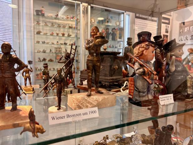 Mehrere Schornsteinfeger-Figuren aus Bronze und Keramik stehen in einer Vitrine, einige mit Leitern und Zylindern.