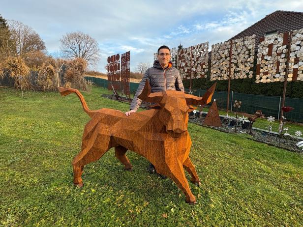 Ein Mann steht im Garten neben einer großen, eckigen Skulptur eines Stiers aus rostigem Metall.
