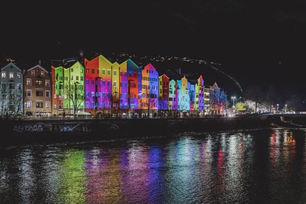 Bunte Häuserfassaden in Innsbruck spiegeln sich nachts im Wasser.