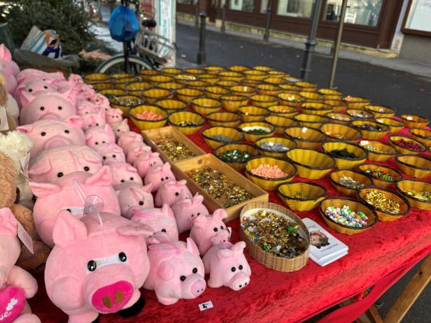 Mehrere rosa Plüschschweine und zahlreiche Körbchen mit bunten Glücksbringern auf einem Marktstand.