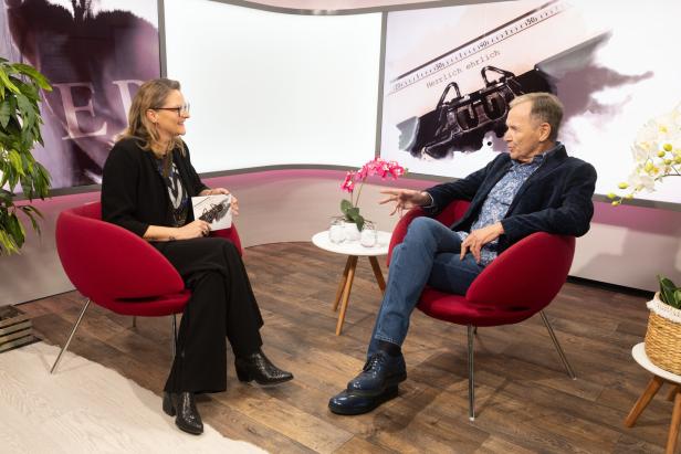 Eine Frau und ein Mann sitzen in roten Sesseln und unterhalten sich vor einem Hintergrund mit Schreibmaschinenmotiv.