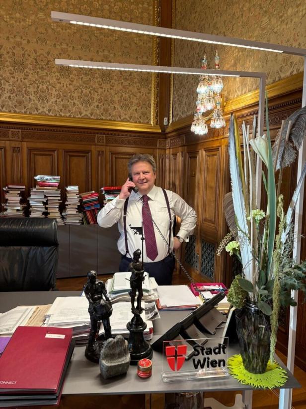 Wiens Bürgermeister Michael Ludwig telefoniert in einem prunkvoll eingerichteten Büro mit vielen Aktenstapeln und Dekoration auf dem Schreibtisch.