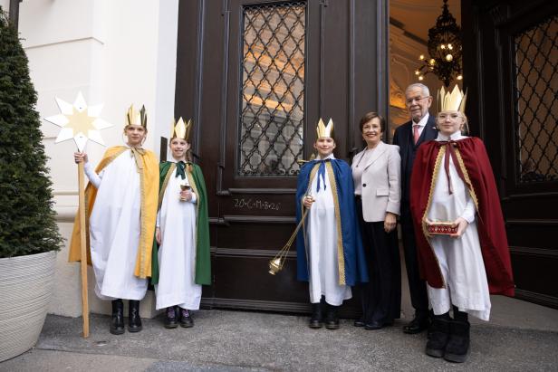 Sternsinger mit Alexander Van der Bellen und seiner Frau vor einer Tür.