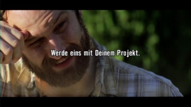 Heimat Berlin Hornbach-TV/Werde eins mit Deinem Projekt Ein bärtiger Mann wischt sich die Stirn; im Vordergrund steht der Text „Werde eins mit Deinem Projekt.“.