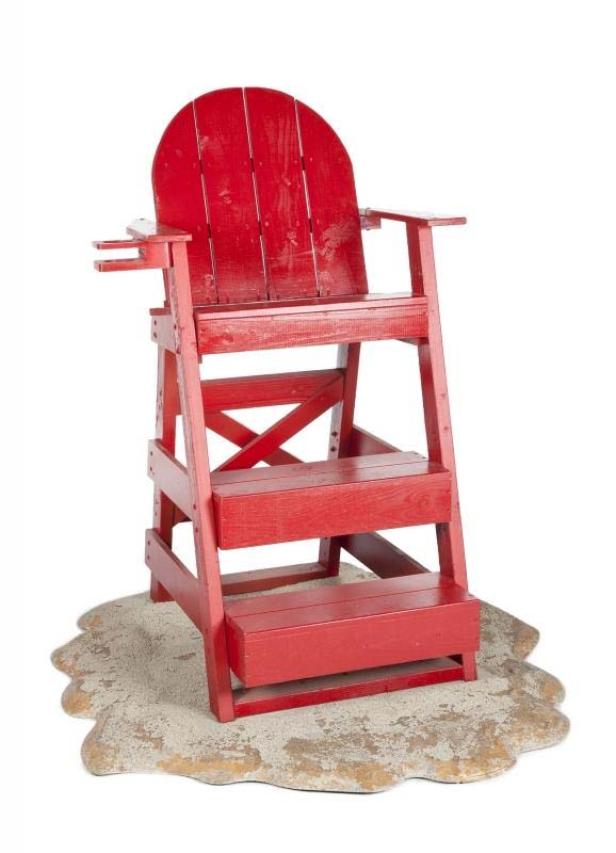 Ein rot gestrichener, hölzerner Rettungsschwimmerstuhl steht auf einem sandfarbenen Untergrund.