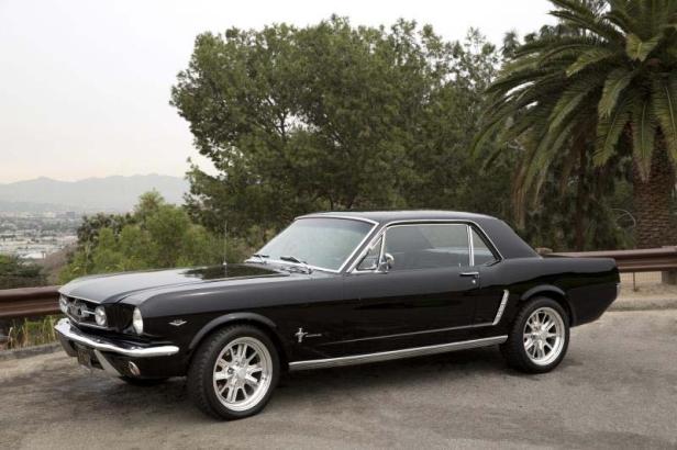 Ein schwarzer Ford Mustang der ersten Generation steht auf einer Straße.