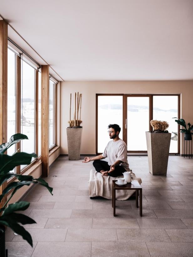 Ein Mann in gemütlicher Loungewear sitzt auf einer Matte in einem Meditationssitz und praktiziert Yoga