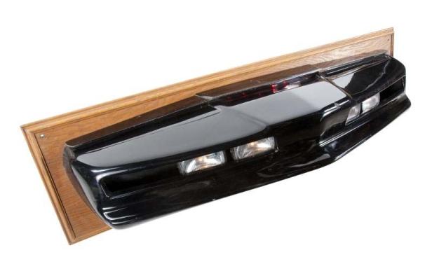 Die Frontpartie von K.I.T.T., dem sprechenden Auto aus der Serie „Knight Rider“, ist an einer Holzplatte montiert.