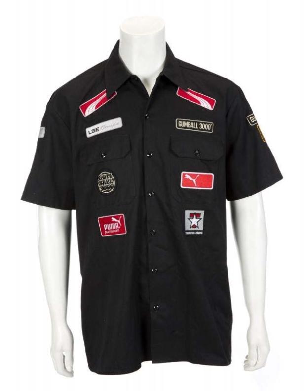 Eine schwarzes Hemd mit verschiedenen Aufnähern, darunter „Gumball 3000“ und Puma-Logos.