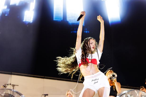 Nina Chuba tanzt auf einer Bühne und hält ein Mikrofon, während im Hintergrund eine Musikerin Trompete spielt.