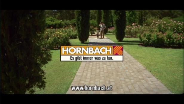 Heimat Berlin Hornbach-TV/Werde eins mit Deinem Projekt Ein Garten mit einem Weg, auf dem ein Mann mit einem Kind und einem Hund spaziert. Im Vordergrund ist das Hornbach-Logo zu sehen.