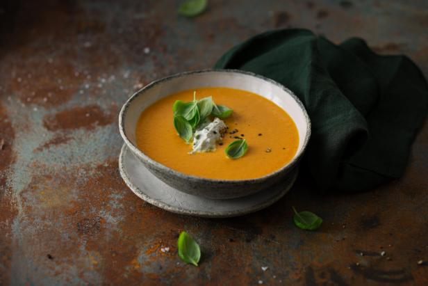 Cremige orange Suppe in einer Schale, garniert mit frischen Basilikumblättern und Pfeffer.