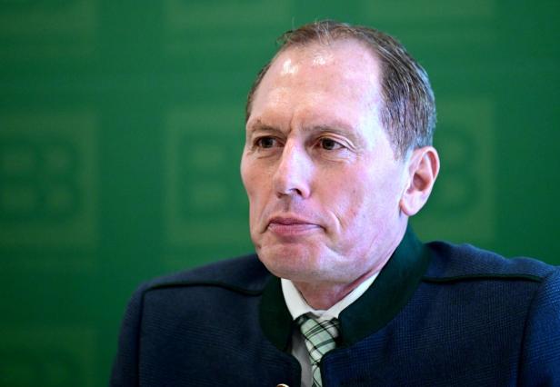 Ein Mann mit Trachtenjacke und Krawatte blickt vor einem grünen Hintergrund zur Seite.