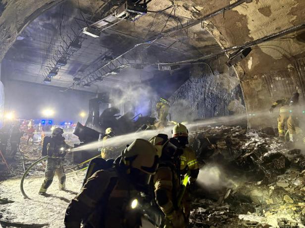 Feuerwehrleute bekämpfen einen Brand in einem Tunnel mit Wasserschläuchen.