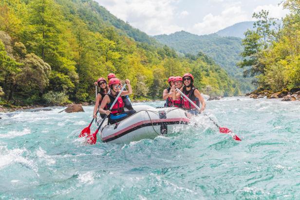 Gruppe beim Rafting auf einem klaren Fluss, umgeben von grünen Bergen und Wäldern.