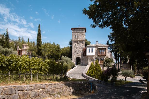 Steinernes Klostergebäude mit Turm, Weinreben und Bäumen unter blauem Himmel.