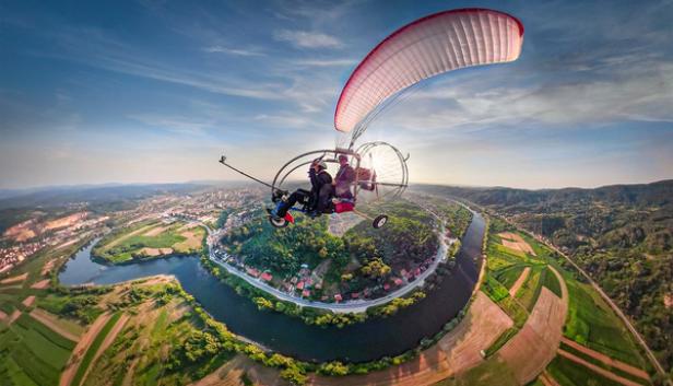 Ein Mann fliegt mit einem Paraglider über einen Fluss.