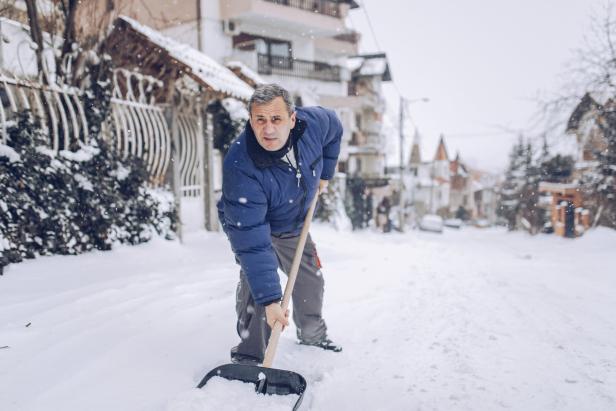 Ein Mann schaufelt im Freien Schnee mit einer Schneeschaufel. 