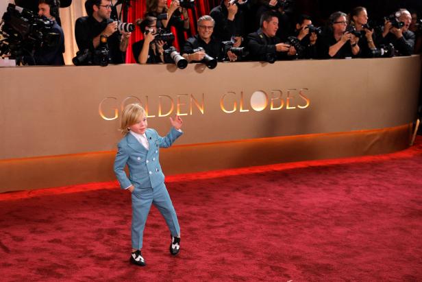 Ein Kind im blauen Anzug posiert auf rotem Teppich vor Fotografen bei einer Preisverleihung.