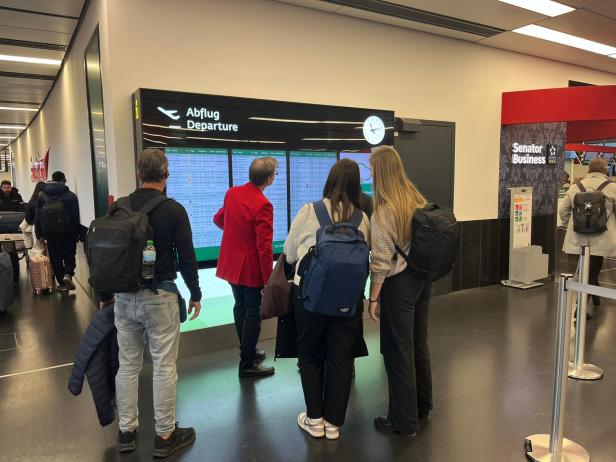 Mehrere Reisende betrachten die Abflugtafel am Flughafen Wien.