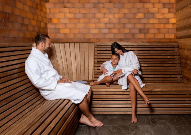 Familie in weißen Bademänteln entspannt gemeinsam in einer modernen Sauna auf Holzbänken.
