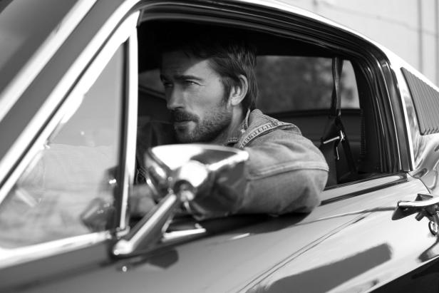 Ein Mann mit Bart schaut aus dem Fenster eines Oldtimers.