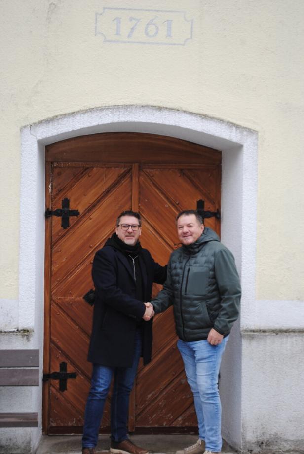 Zwei Männer geben sich vor einer alten Holztür mit der Jahreszahl 1761 die Hand.