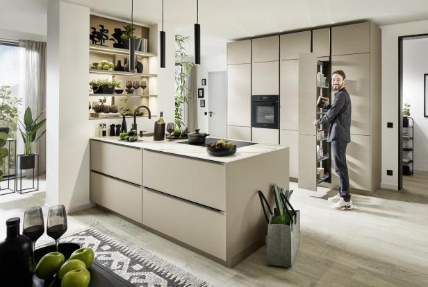 Moderne Küche mit grifflosen Fronten in Beige, viel Stauraum, offenen Regalen, Pflanzen und smarten Details wie ausziehbarem Vorratsschrank und integriertem Backofen.