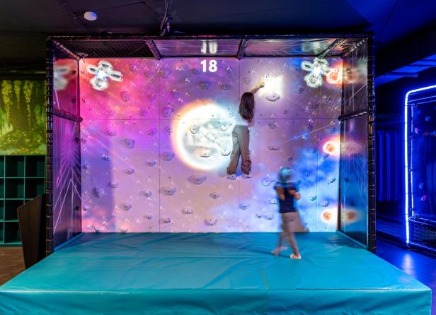 Kinder klettern an einer interaktiven, bunt beleuchteten Kletterwand in einer Indoor-Abenteuerwelt.