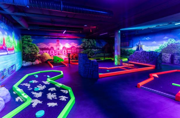 Bunte Indoor-Minigolfanlage mit leuchtenden Bahnen und fantasievoller Wandmalerei.