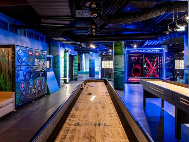 Bunte Indoor-Abenteuerwelt mit Spielgeräten, Rutschen und Shuffleboard-Tischen.