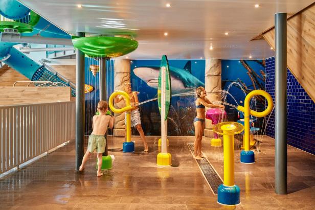 Kinder spielen in einem bunten Indoor-Wasserspielbereich mit Wasserspritzgeräten.