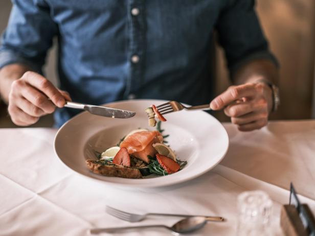 Ein Teller mit Lachs, Brot, Erdbeeren und Gemüse auf einem weiß gedeckten Tisch.