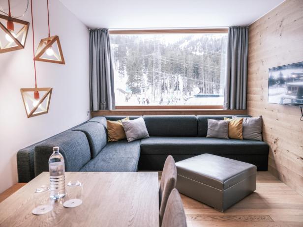 Modern eingerichtetes Hotelzimmer mit großer Fensterfront und Blick auf verschneite Skipiste.