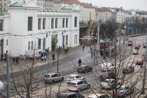 Viele Autos stehen im Stau vor einer U-Bahn-Station, während zahlreiche Menschen auf dem Gehweg unterwegs sind.