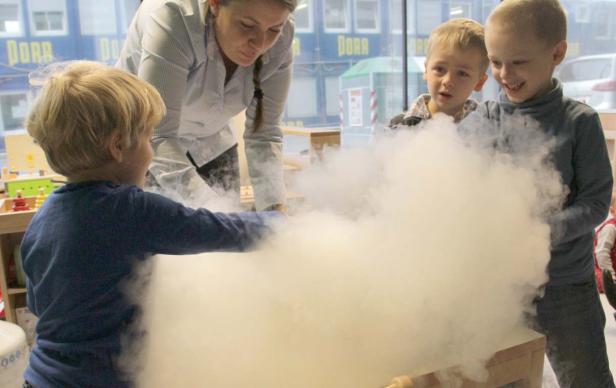 Kinder und eine Frau beobachten dichten Nebel in einem Innenraum.