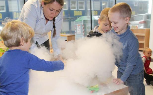 Eine Frau und drei Kinder experimentieren mit Trockeneis und erzeugen Nebel.