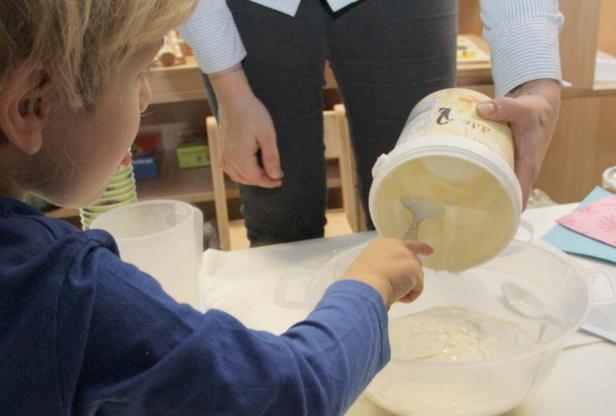 Ein Kind hilft beim Auslöffeln von Teig in eine Schüssel.