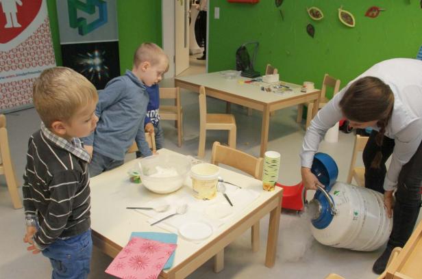 Kinder beobachten, wie eine Frau mit flüssigem Stickstoff experimentiert.