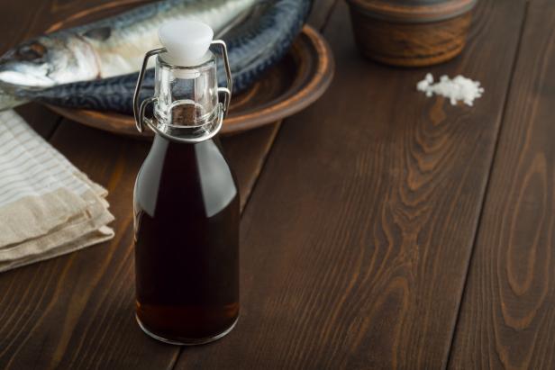 Auf einem Holztisch stehen eine Flasche dunkler Flüssigkeit, ein Teller mit Fisch und etwas Salz.